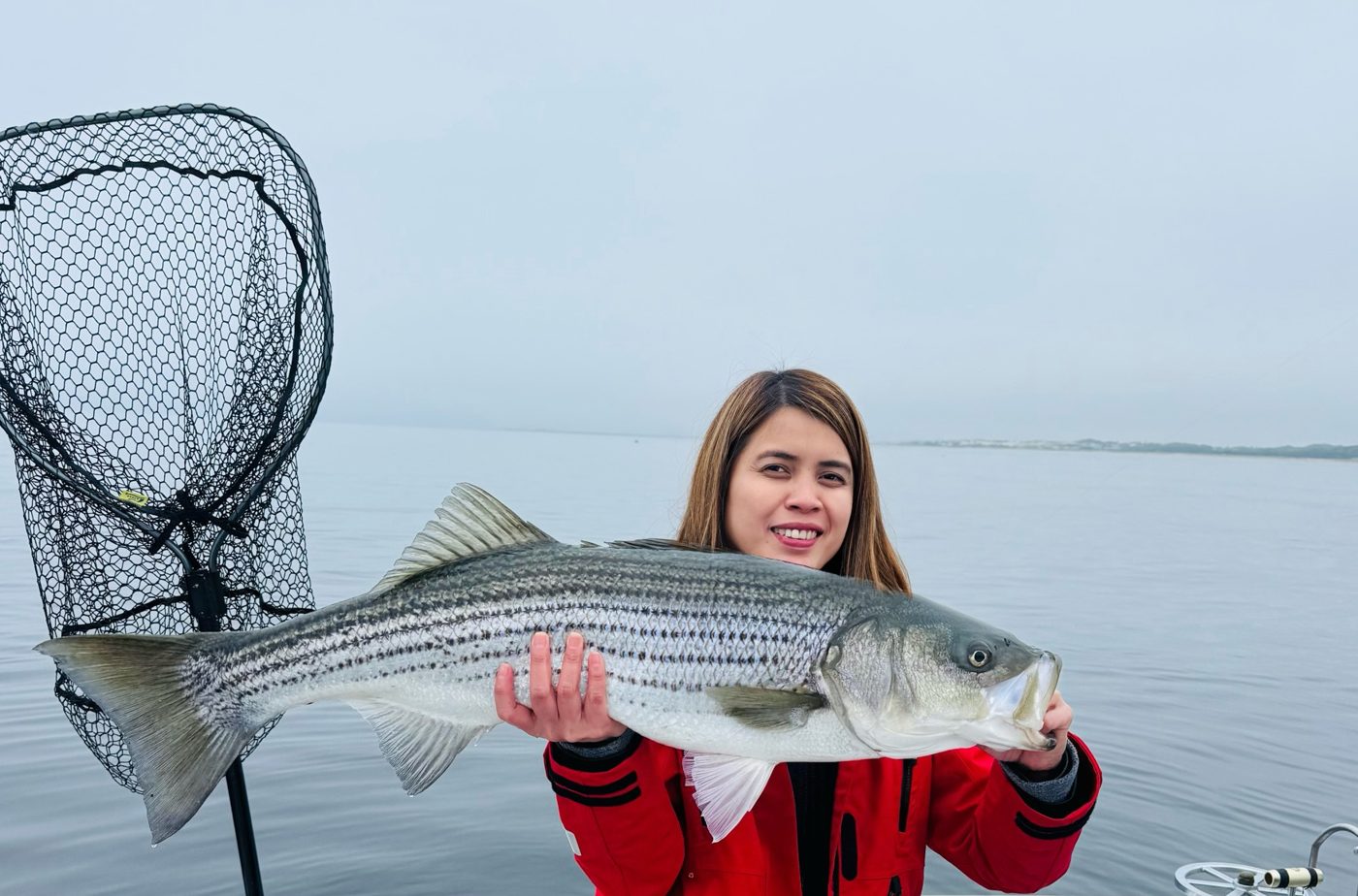 Arlyn Mitchell, co-owner of Outdoor Property Services, holding up a striped bass on the water