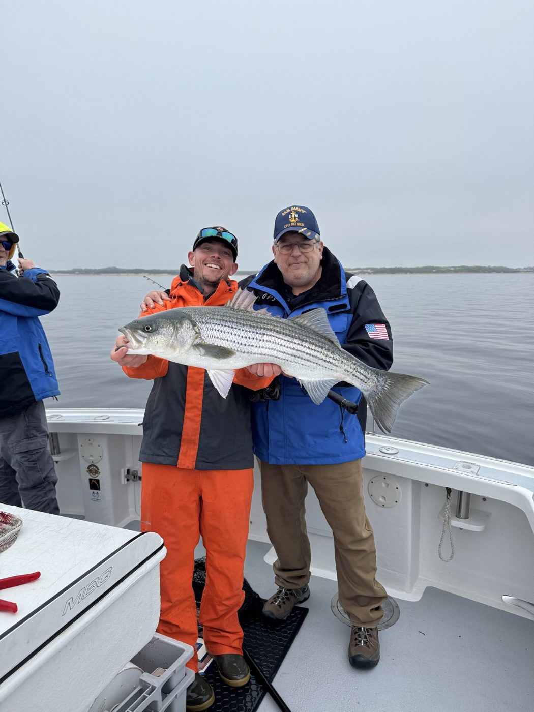 William Mitchell, owner of Outdoor Property Services, in a Navy cap holding a striped bass on the water with a friend