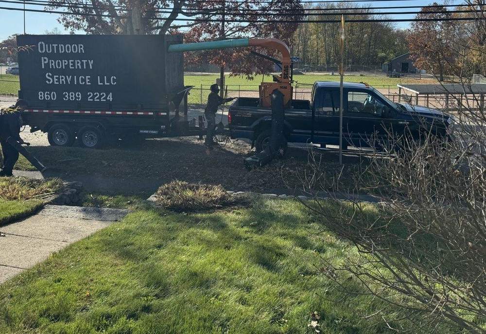The lettered Outdoor Property Services leaf box trailer and truck loader at the curb on a fall morning