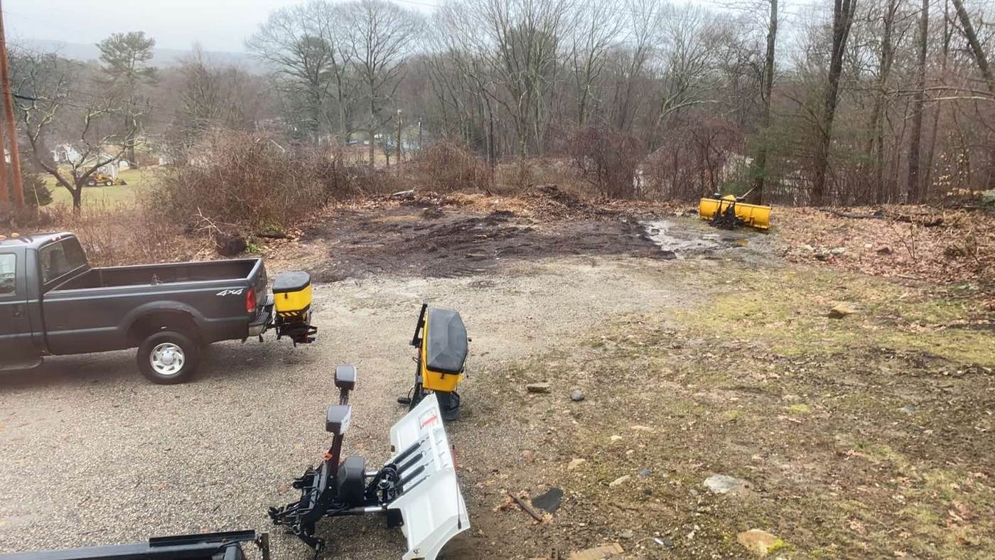 Ground cut back to bare soil on a clearing job in southeastern Connecticut, the cut growth piled off at the edge and the equipment on site
