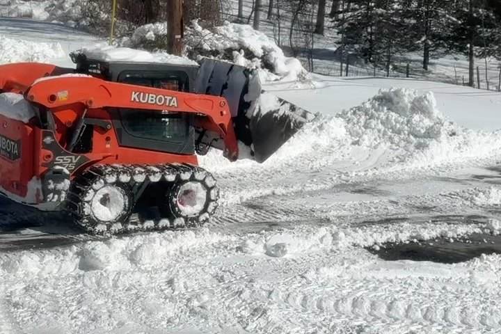 A tracked skid steer stacking a snow pile clear of the paved area