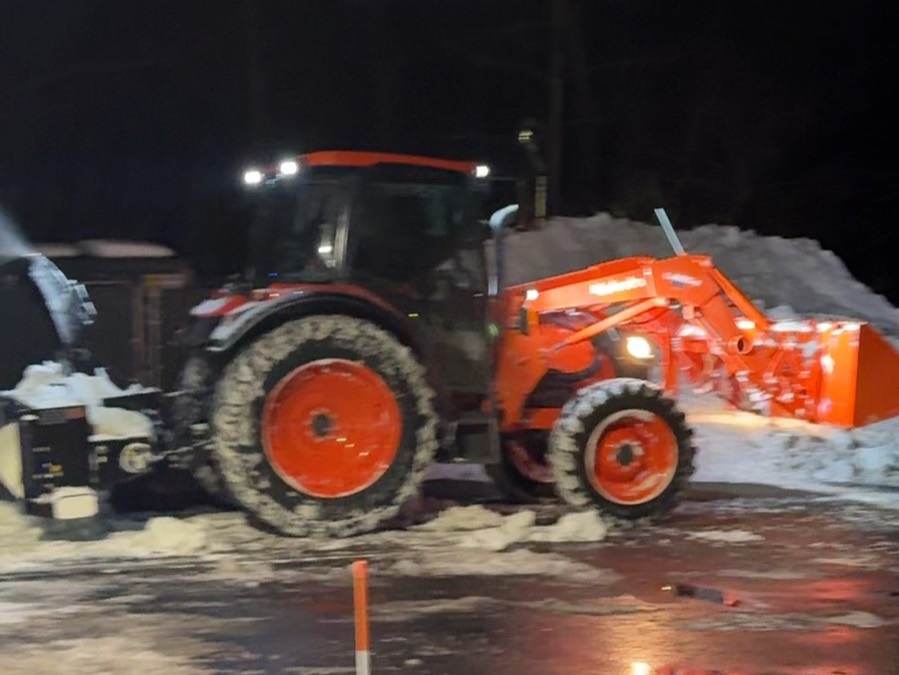 An Outdoor Property Services tractor with a front loader beside a snow pile in a commercial lot at night