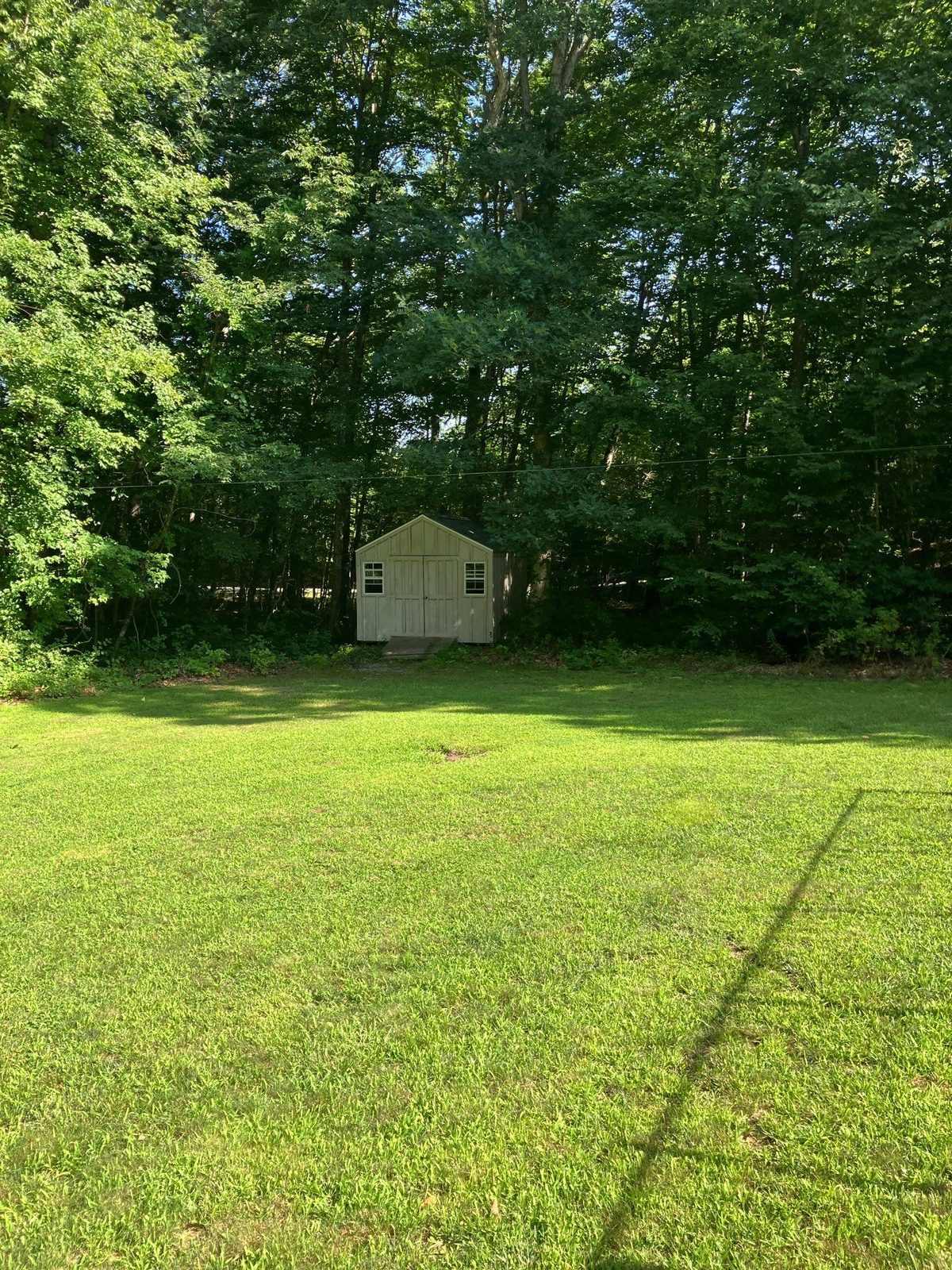A back lawn cut clean to the woods edge behind a shed on a property in southeastern Connecticut, mown by Outdoor Property Services