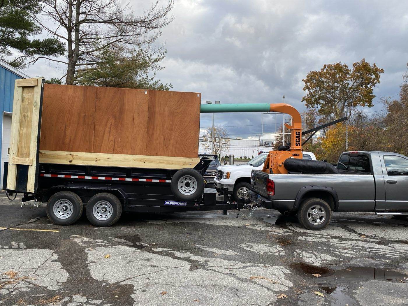 The Outdoor Property Services leaf box trailer with the truck loader and its intake hose, hitched behind a pickup on an autumn afternoon
