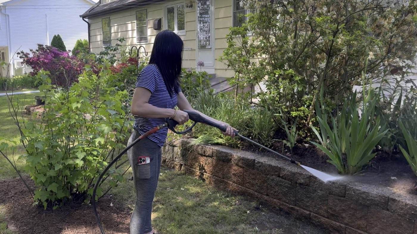 An Outdoor Property Services crew member pressure washing a block wall beside a planted bed
