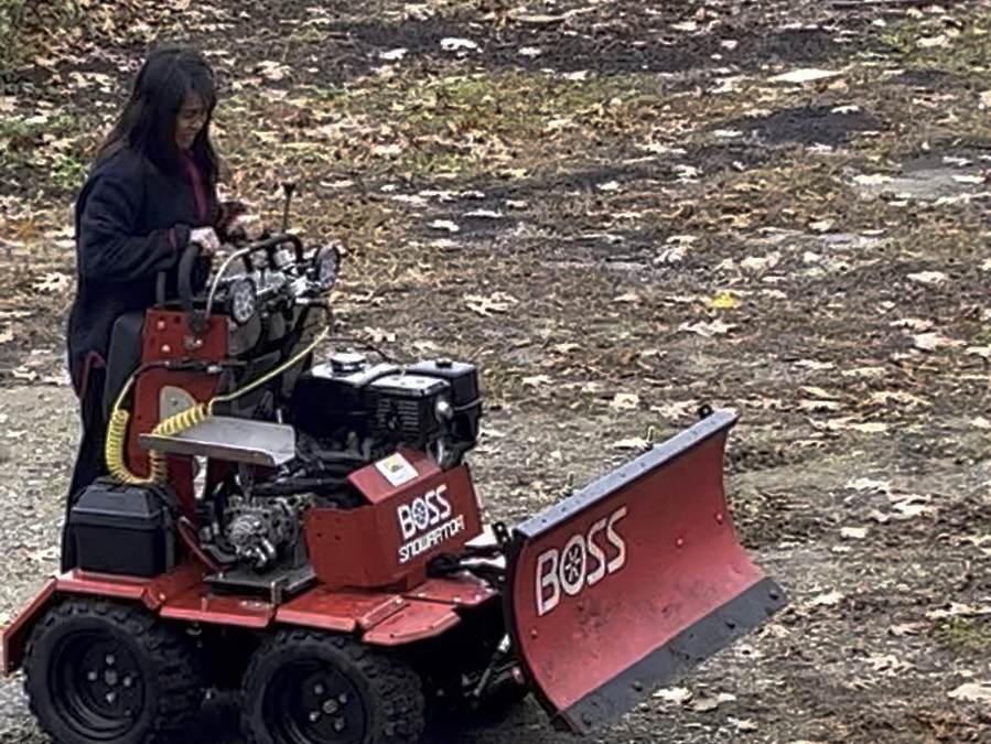 An Outdoor Property Services operator on a Boss stand-on plow machine with the blade angled, on a gravel drive