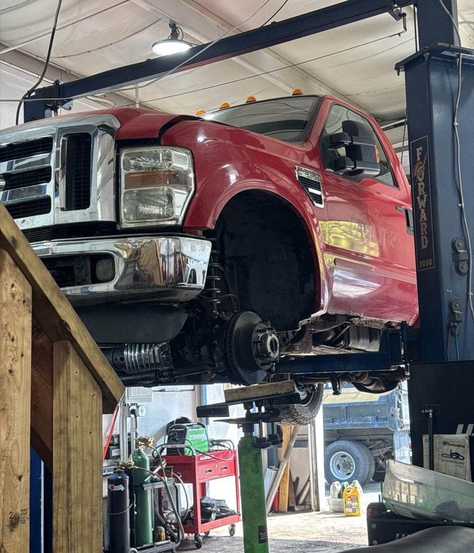 The red Outdoor Property Services F-350 up on the two-post lift in the Groton shop with a wheel off