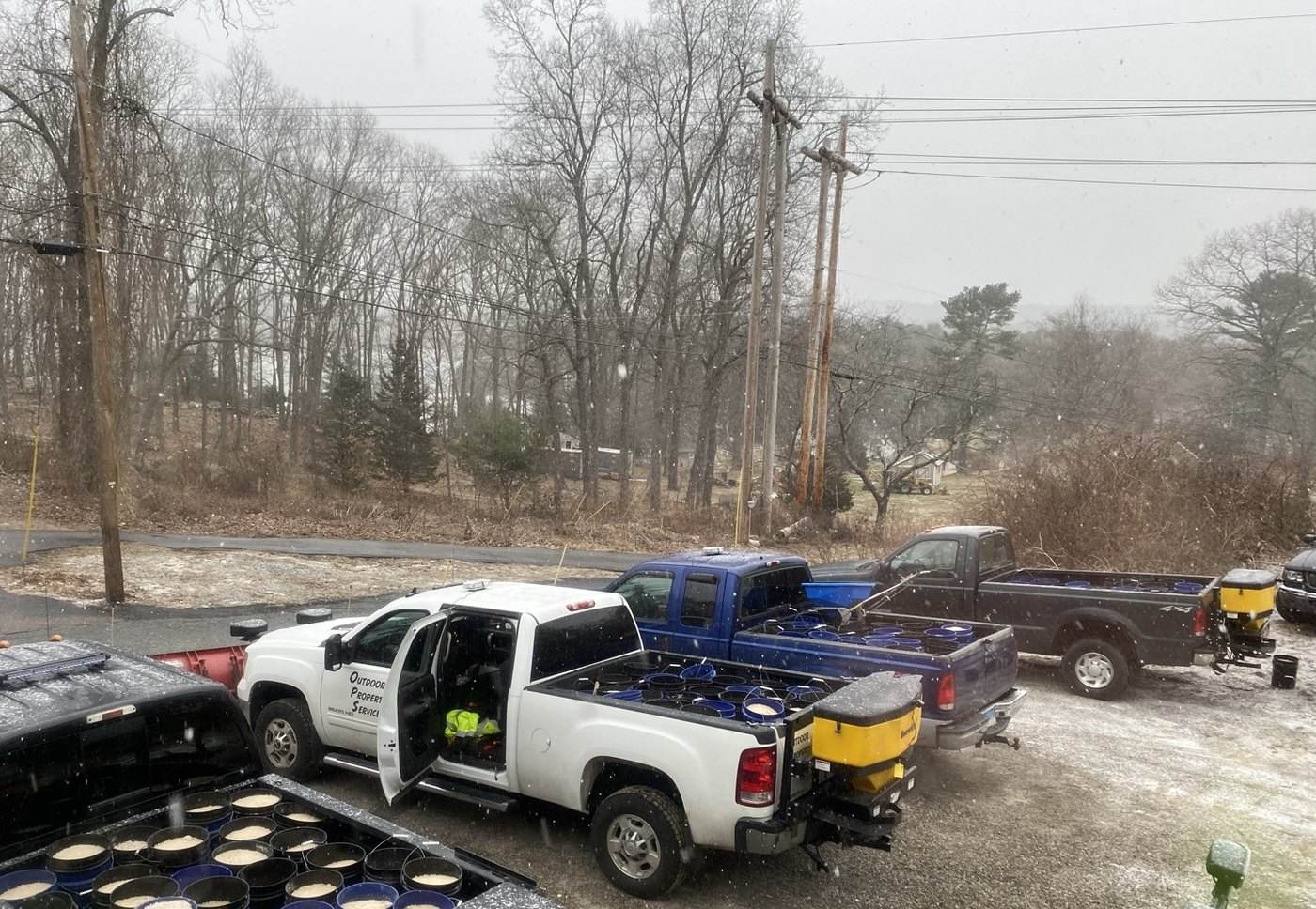 Outdoor Property Services trucks loading de-icing material in the Groton yard in falling snow