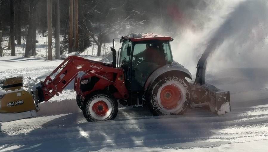 An Outdoor Property Services tractor throwing a plume of snow broadside on a cleared road